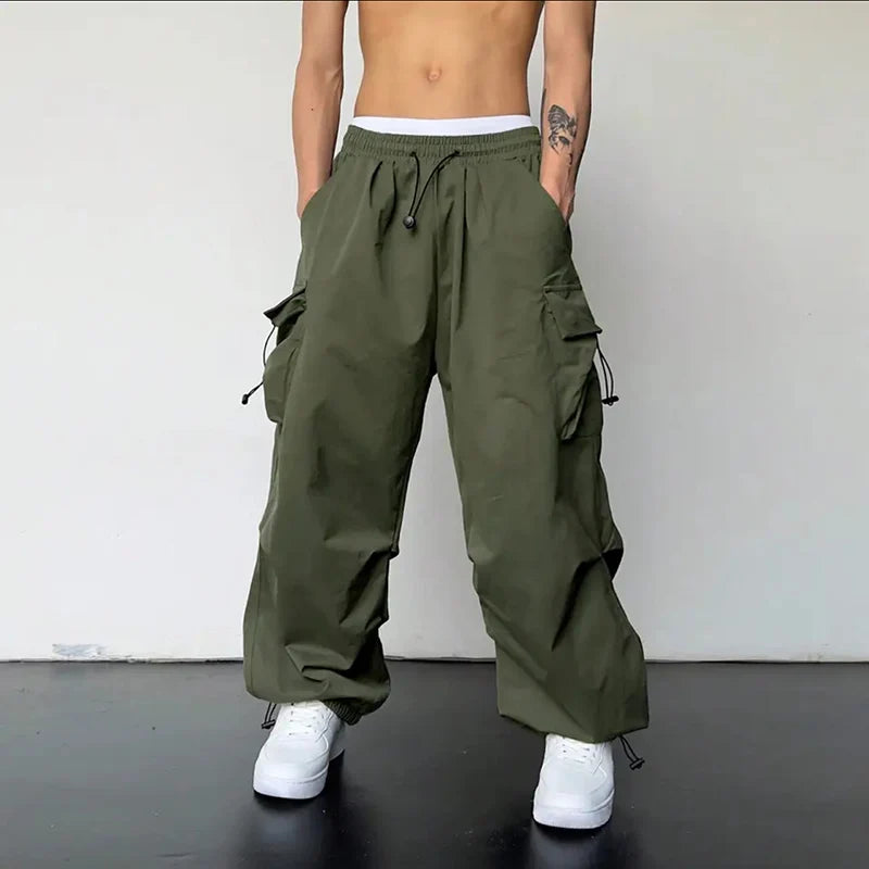 Les pantalons cargo décontractés olive pour hommes, avec plusieurs poches latérales et une taille à cordon de serrage, conçus pour un usage lié à l’habillement de rue.