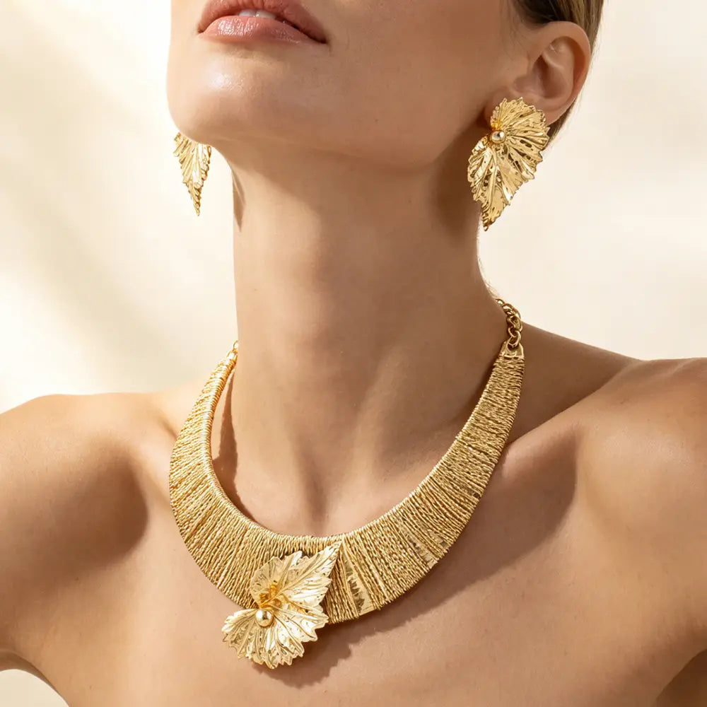 Parure de bijoux en perles et feuilles d’or, comprenant un collier ras du cou inspiré des feuilles d’or, avec un motif tissé texturé et un pendentif central orné.