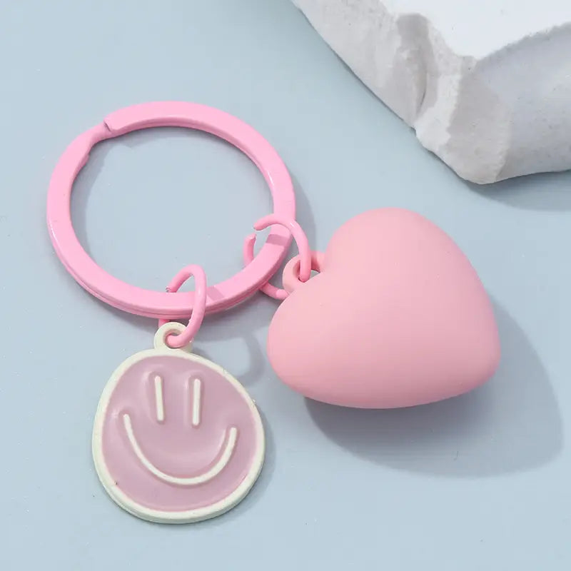 Pink plastic keychain featuring a heart-shaped charm and a smiley face pendant titled pink heart smiley face keychain.