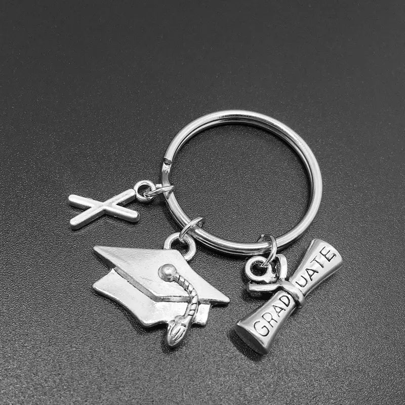 Silberner Schlüsselanhänger zur Abschlussfeier mit einem Anhänger in Form des Buchstabens x, einer Quaste an der Abiturmütze und einem mit Graduate gravierten Diplom-Anhänger.