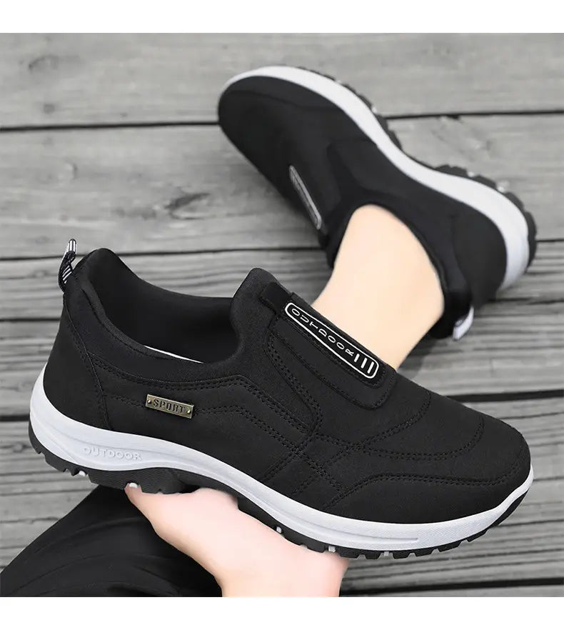 Men orthopedic slip-on walking shoes in black feature a breathable mesh upper with subtle branding and a white rubber sole with textured tread for enhanced comfort and support.