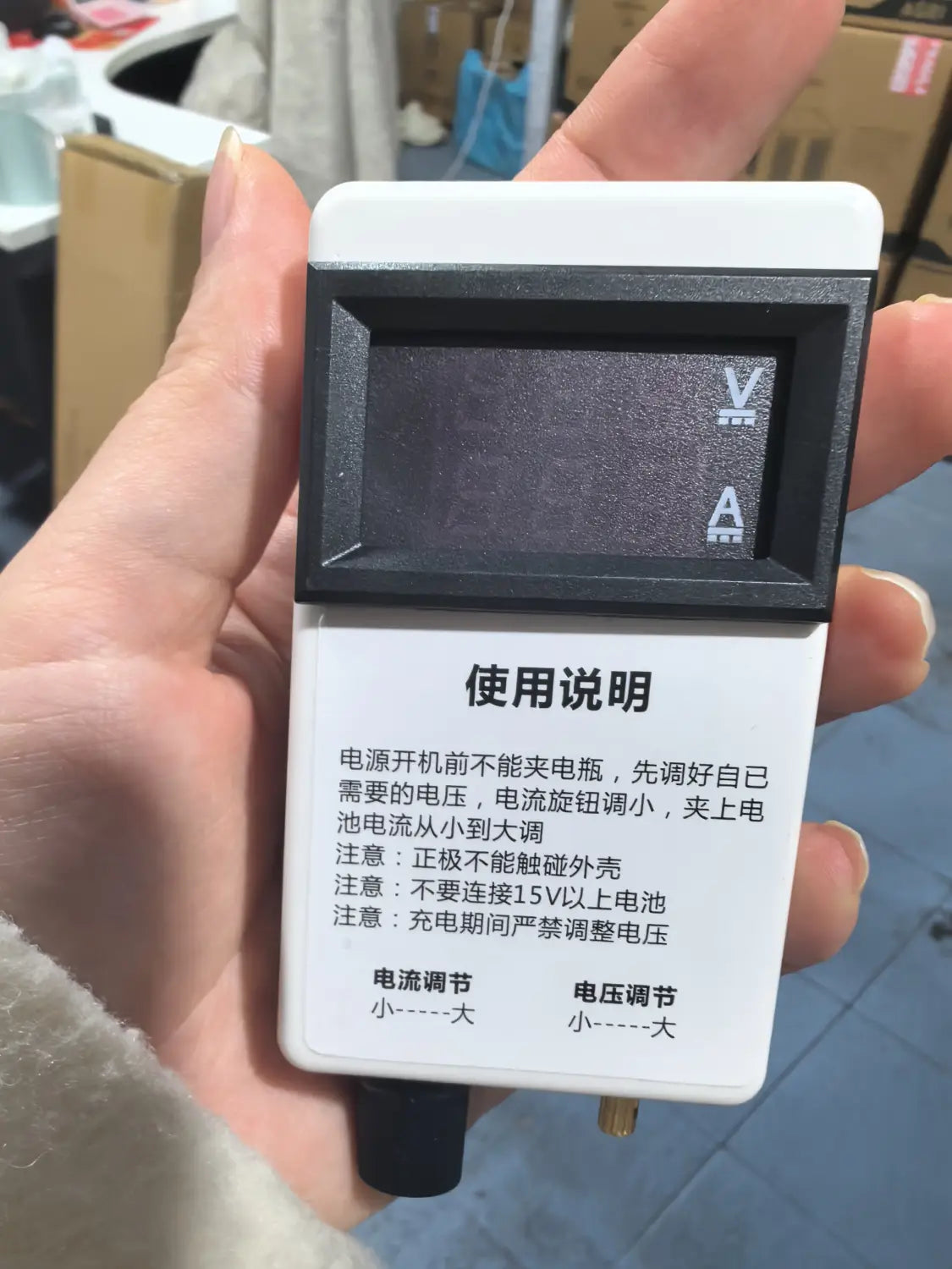 Multimètre de type régulateur de courant et de tension numérique portatif blanc avec écran noir et indicateurs de tension et d’intensité indiqués pour des mesures de 50 A, 60 A, 100 A.