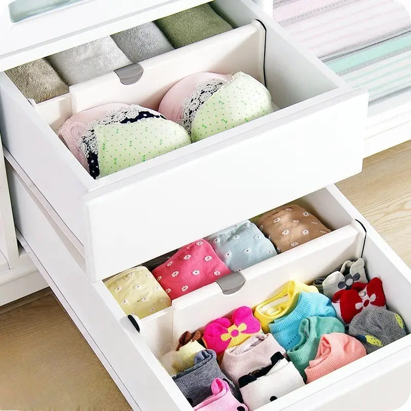 Cloison de tiroir en plastique blanc avec des compartiments segmentés réglables permettant d’organiser avec soin le linge de dessous et les chaussettes pliés.