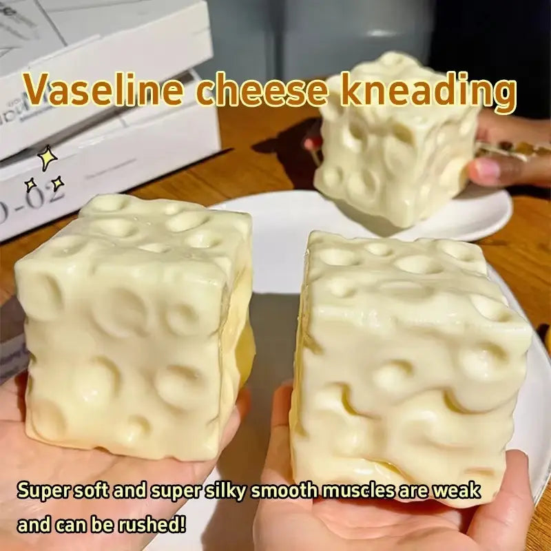 juguete de alivio del estrés de color crema con forma de cubo y superficie texturizada, con orificios que recuerdan al queso suizo, mostrado desde el frente, que evidencia su diseño de queso en forma de juguete blando de crecimiento lento.