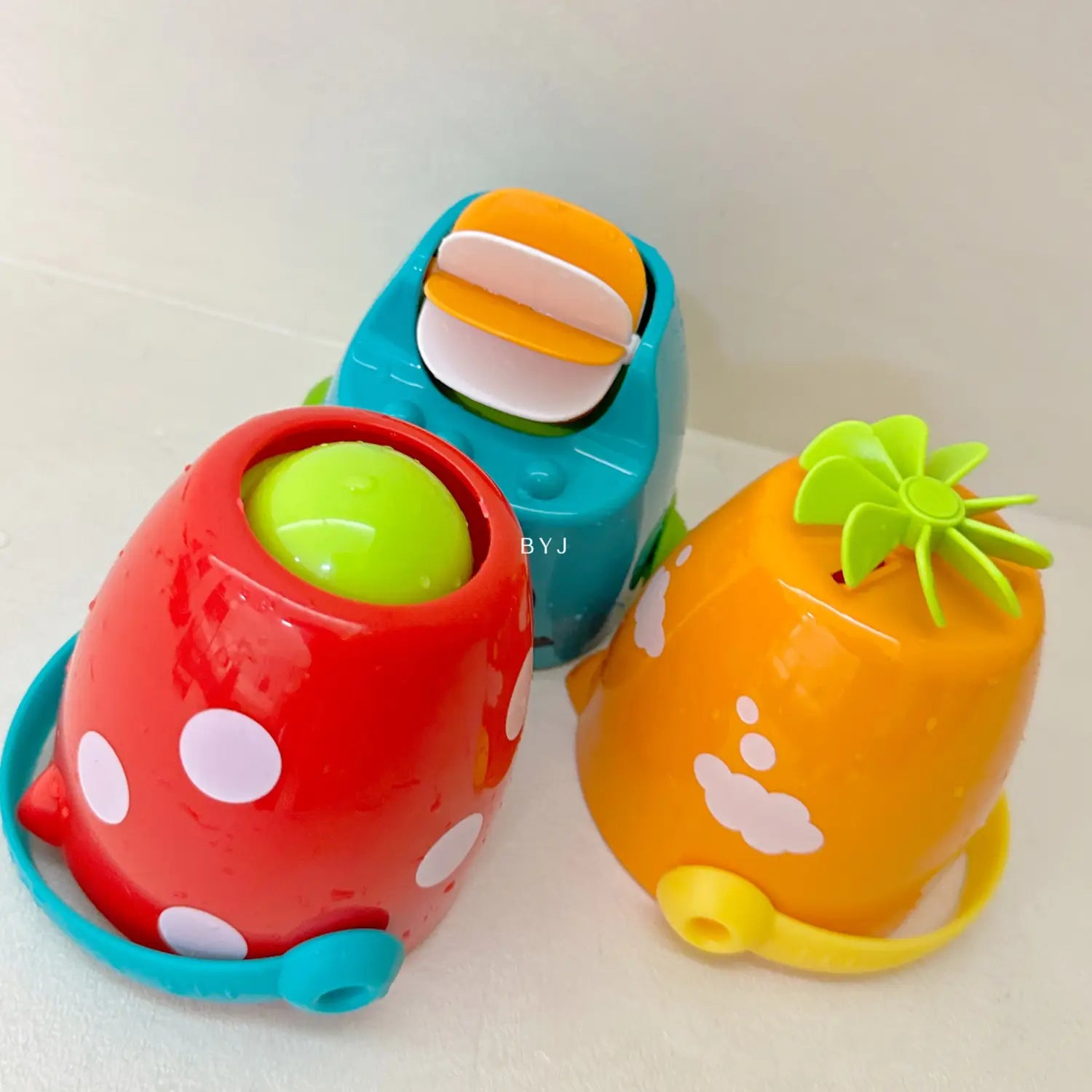 Leuchtend bunte Kunststoff-Badewannen-Eimer für Babys mit Wassersprühfunktion, geformt als Erdbeere, Blaubeere und Karotte; mit verspielten Punkten und blättrigen Oberseiten.