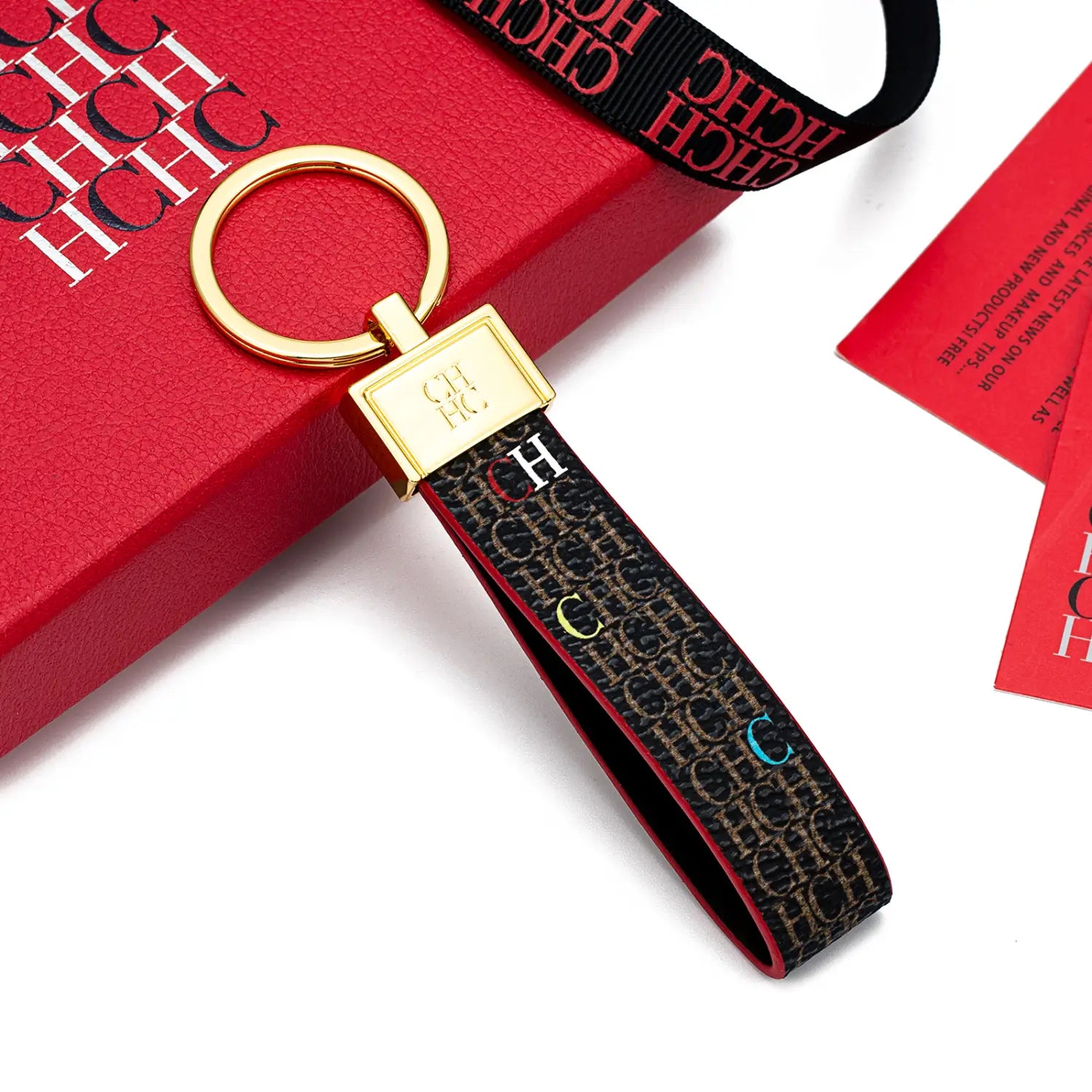 Leather logo keychain featuring a gold-toned key ring and a black fabric strap with a repeating ch monogram in beige accented by small colorful letters.