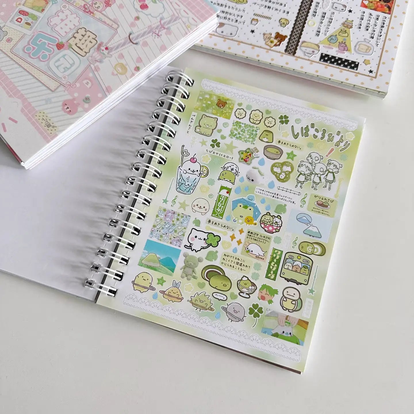 Ein spiralgebundenes Notizbuch mit leicht grünem Umschlag, verziert mit Kawaii-Pastellstickern, die Charaktere und Szenen aus „Kawaii Kpop Sticker Book Spiral Journal Stationery“ zeigen.