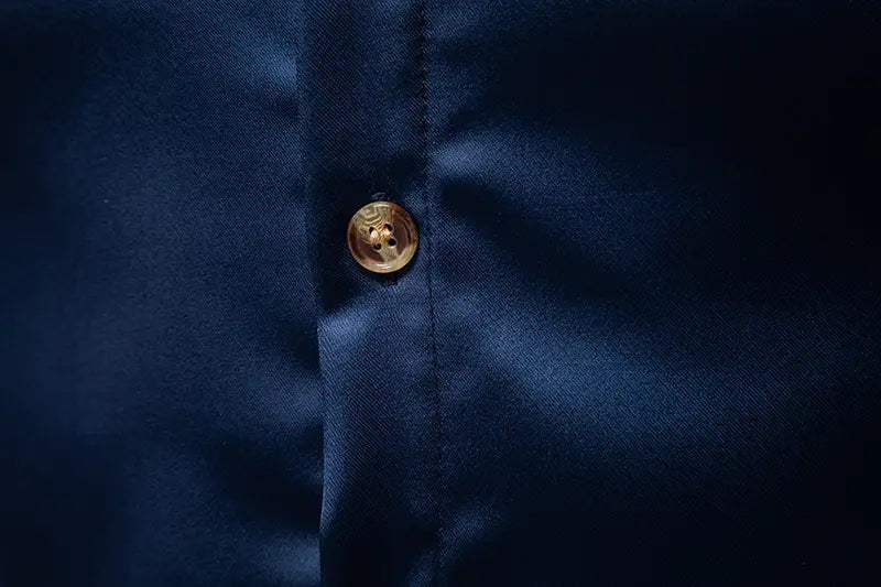 Ein Herrenhemd mit goldfarbenem Besatz aus Satin mit einem runden goldfarbenen Knopf mit subtiler, strukturierter Musterung auf dunklem navyblauem Stoff.
