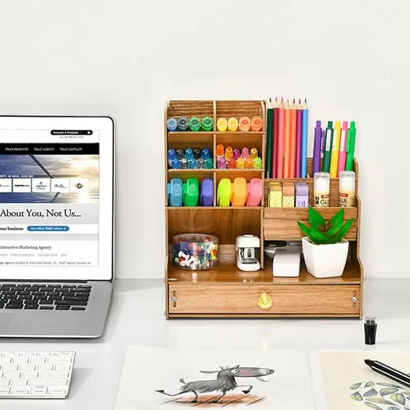 Wooden desk organizer with drawer featuring multiple compartments holding colorful markers pencils glue sticks and a small potted plant.