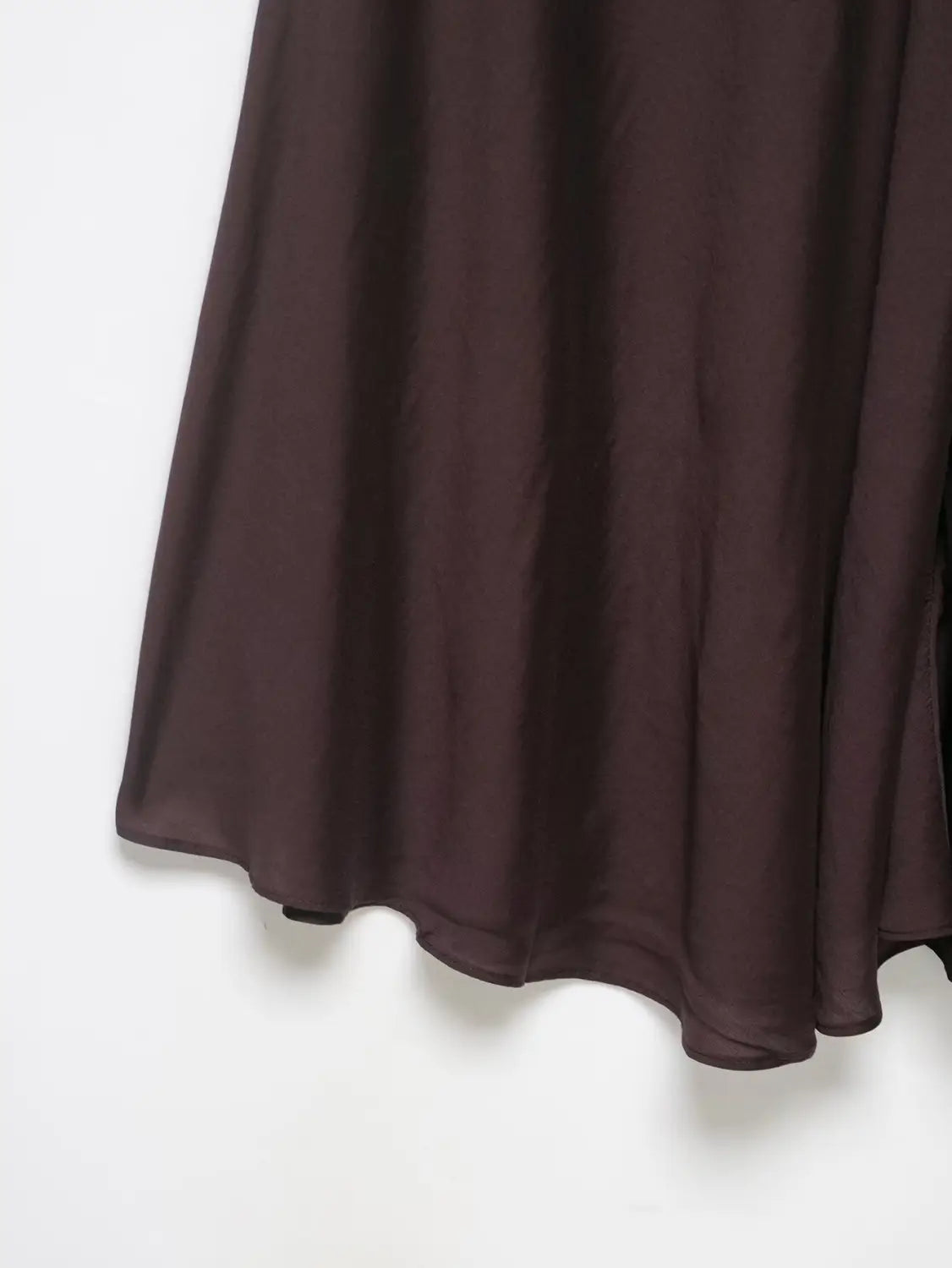 Ein fließender dunkelbrauner Satin-Plisseerock im Midi-Format mit hoher Taille und gesäumtem, geschwungenem Saum aus glattem, leichtem Material.