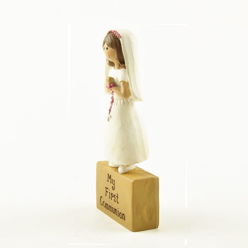 figurine en résine blanche d’une jeune fille en tenue de communion avec un voile et un serre-tête rose tenant des perles de chapelet pour la décoration de table de première communion.