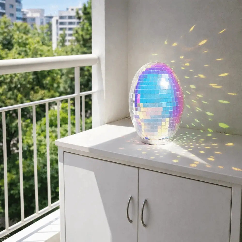 An iridescent glass disco egg ball ornament featuring a shimmering mosaic of rainbow-hued tiles reflecting light.