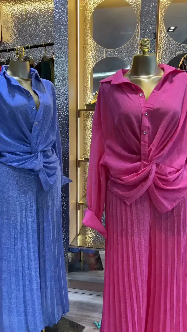 Ein lebhaftes pinkfarbenes Falten-Maxikleid mit Knopfkragen und vorderem Knotendetail, präsentiert im Damen-Set mit Faltenrockhose im weitem Bein, bestehend aus einem langärmeligen Outfit.