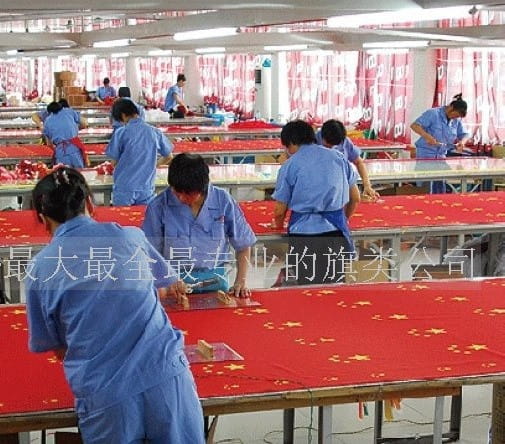 Arbeiter montieren roten Stoff mit gelben Sternmustern für eine Deutschland-Flagge mit Stangenhülse in einer Fabrikumgebung