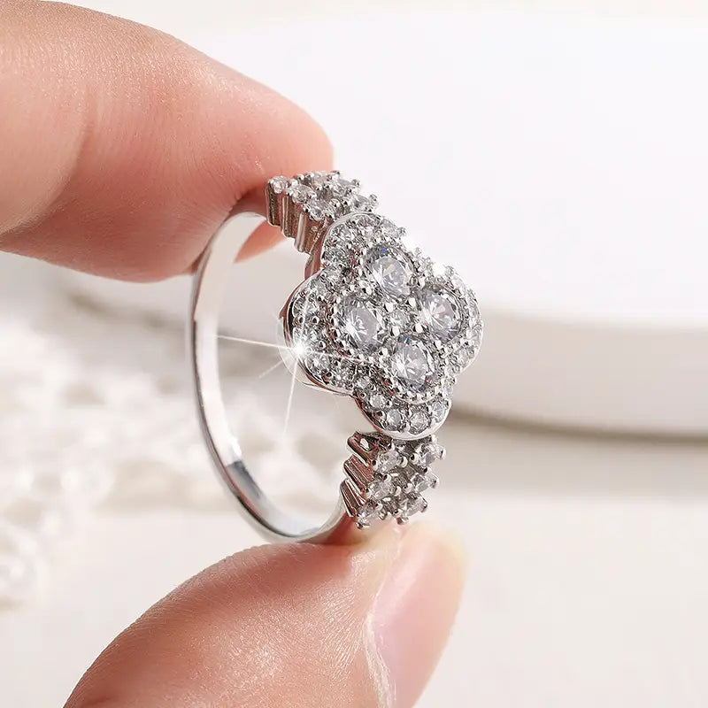 Un anillo de trébol de cuatro hojas de plata con brillo, adornado con múltiples piedras de diamante facetadas transparentes.