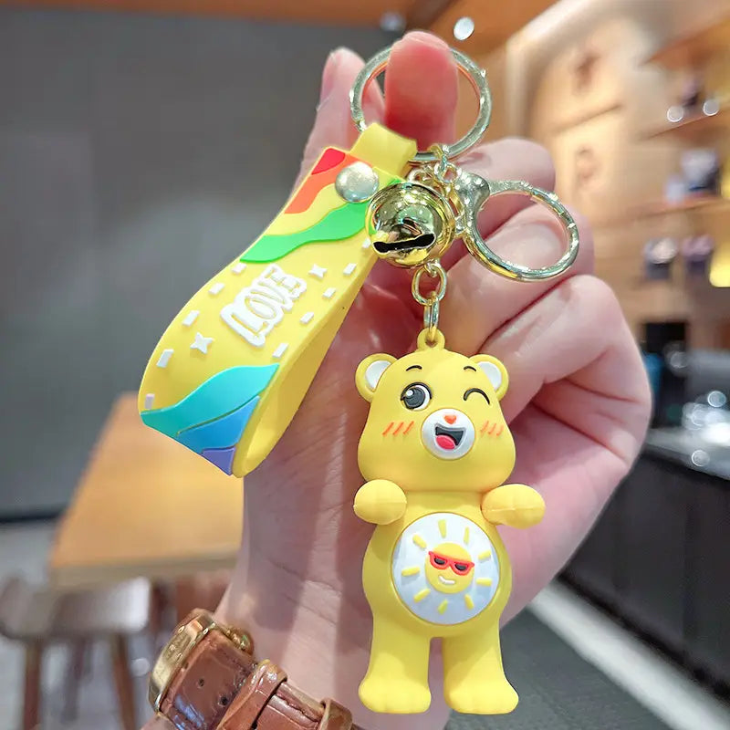 Yellow care bear silicone keychain with rainbow strap and bell designed as a cartoon backpack pendant.