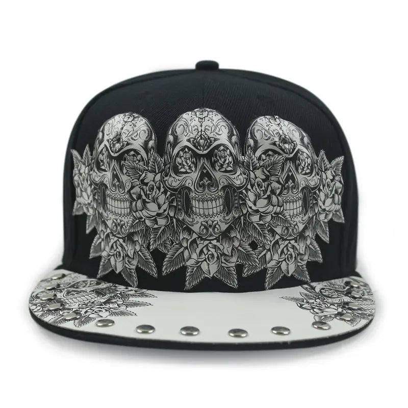 Black snapback baseball cap featuring a detailed silver sugar skull and rose design on the front with a matching patterned brim accented by metallic studs.