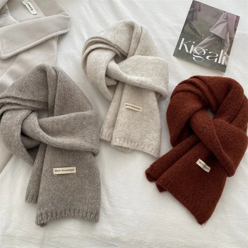 Tres bufandas tejidas en gris claro, gris medio y óxido cálido, con bordes acanalados y etiquetas de encargado de la casa cálidas mostradas como bufanda de invierno tejida en rojo para hombres y mujeres