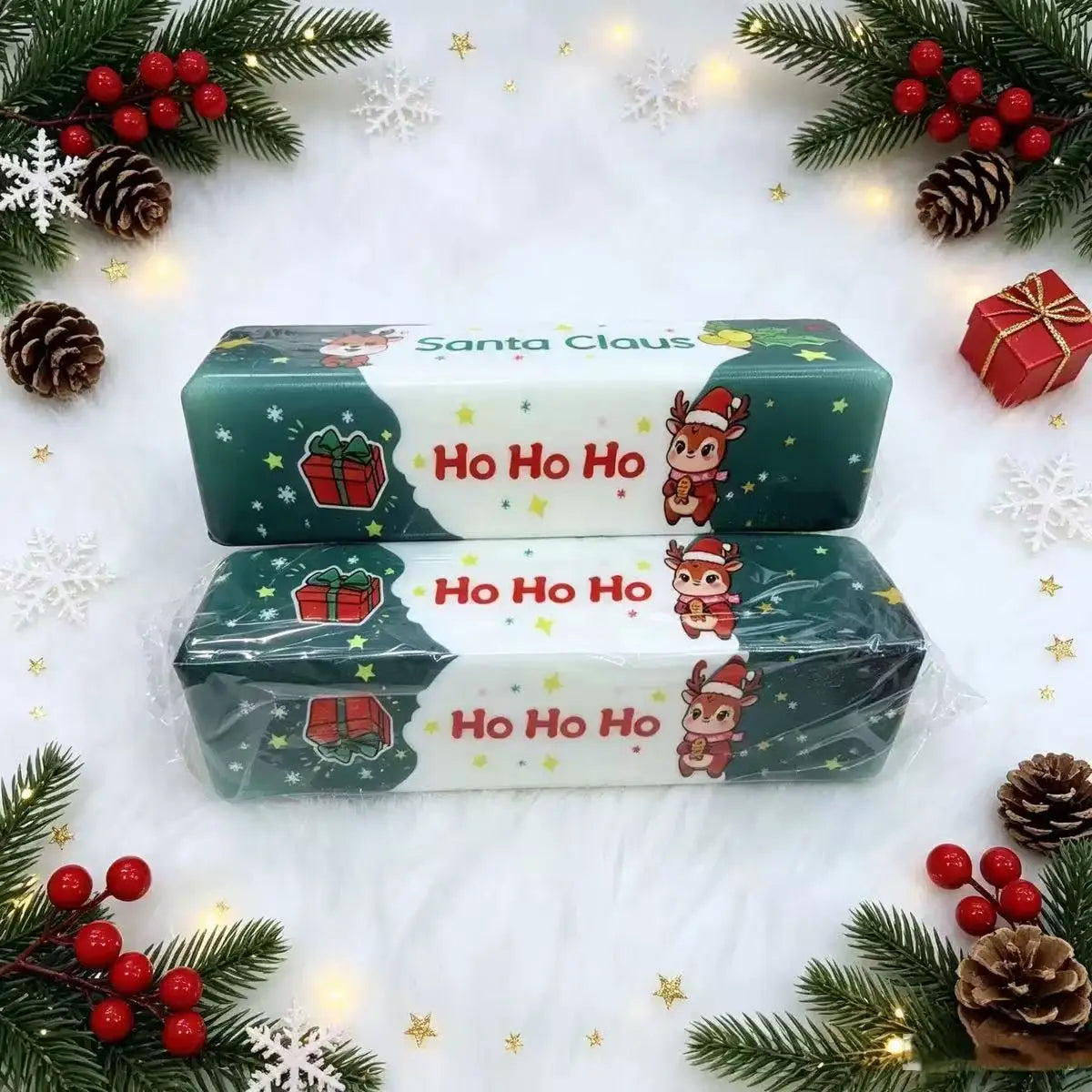 Dos barras rectangulares de juguete de mantequilla blanda y esponjosa festivo en verde y blanco, con un reno caricaturesco y alegre que lleva un gorro de Santa con un «ho ho ho» en letras rojas, como juguete blando de descompresión lenta para aliviar el estrés navideño, juguete navideño festivo de descompresión lenta