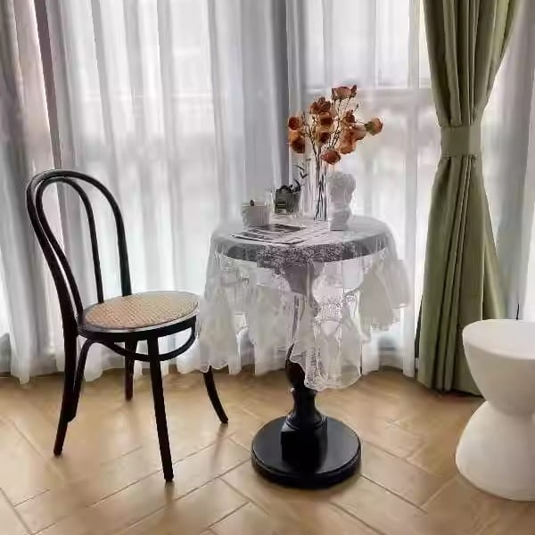 black wrought iron chair with woven wicker seat shown from the back side next to a black wooden pedestal round accent table