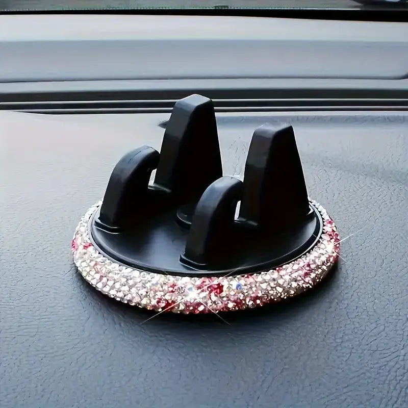 Un soporte negro para teléfono de automóvil con ventilación, de pedrería, con una base circular adornada con pedrería brillante en rosa y transparente.