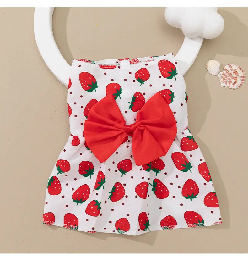 A white strawberry patterned floral dog princess dress with a large red bow at the front.