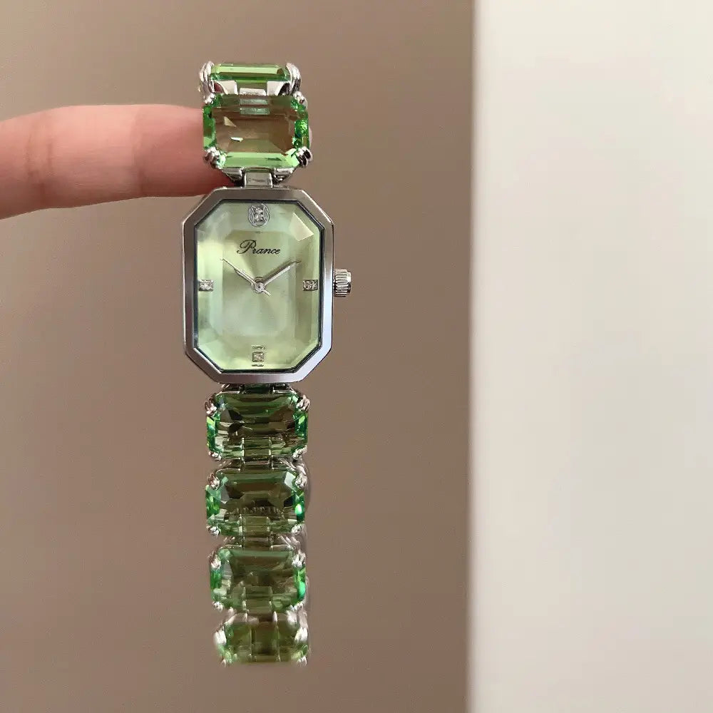 A women quartz crystal watch with a delicate emerald-green faceted gemstone dial and a silver-toned octagonal case and matching bracelet.