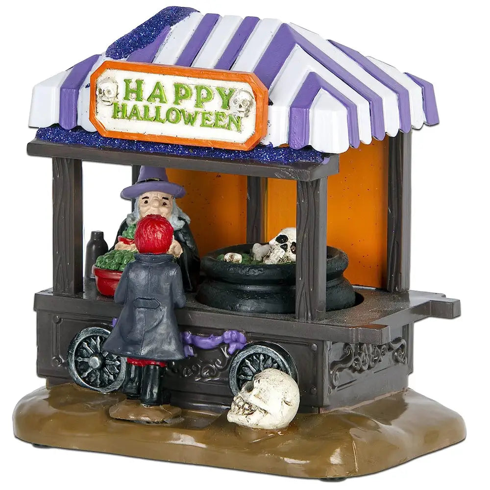 Figurine décorative Halloween en pot à soupe roulant, avec auvent rayé violet et blanc et bordure bleue scintillante au-dessus d’une enseigne orange joyeuse d’Halloween, ainsi qu’une vendeuse sorcière proposant des citrouilles et des crânes, 5 x 14 cm.