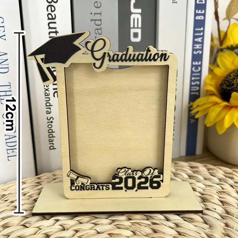 Portarretratos de graduación de madera de tono claro con birrete negro troquelado con láser y guion de graduación, con la clase de 2026 y «felicitaciones» grabados en la base, en un conjunto de portarretratos de graduación de madera de la clase de 2026.