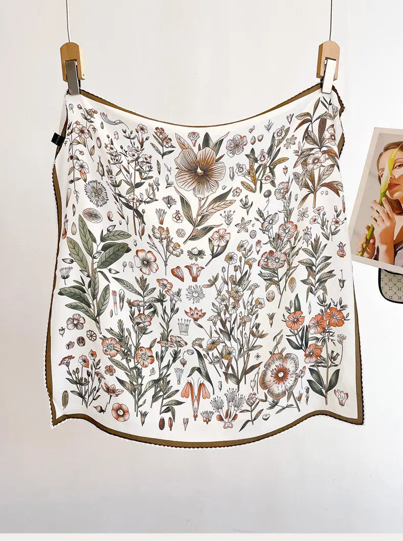 A delicate white silk floral square scarf featuring an intricate botanical illustration in soft earthy tones with detailed linework and a subtle brown border.