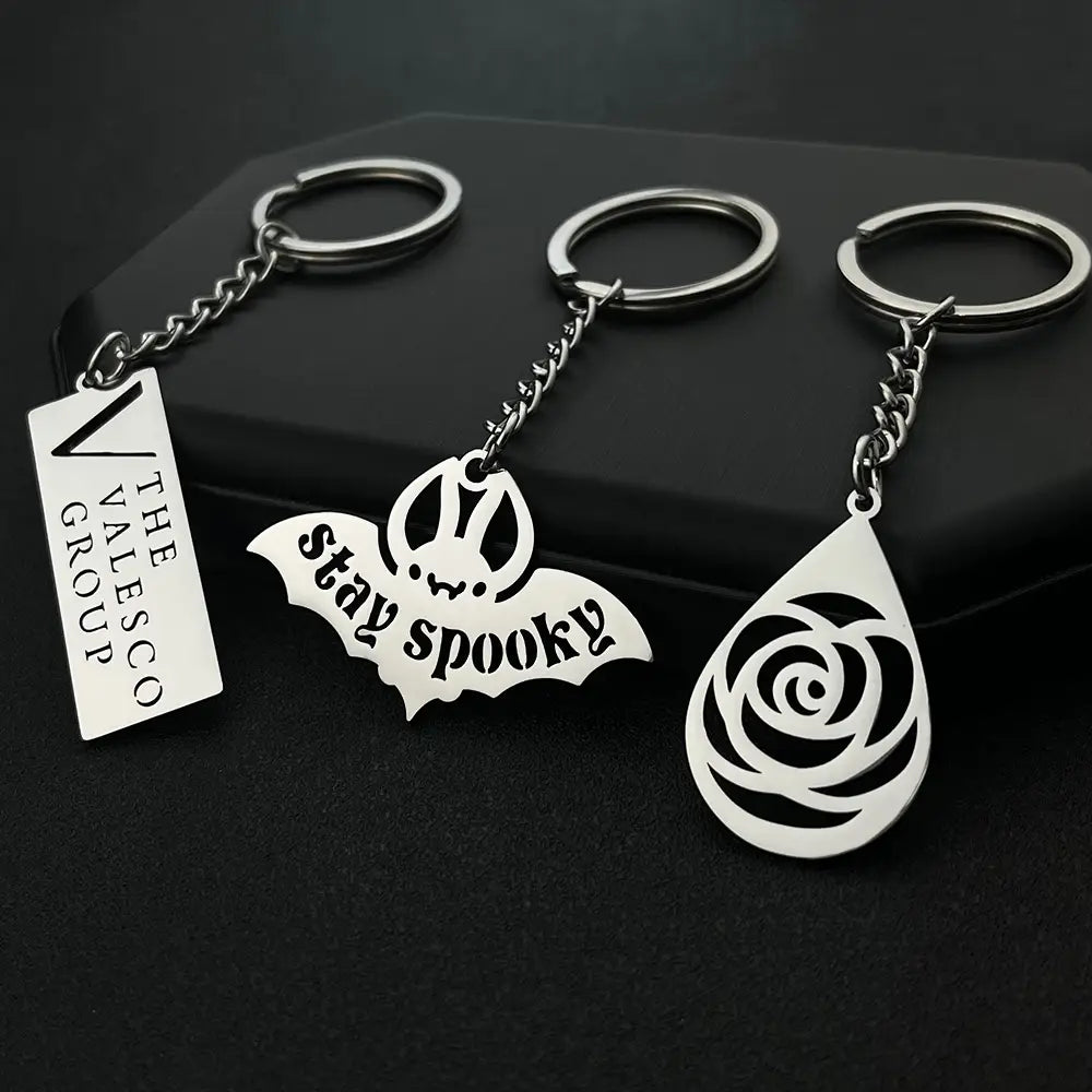 three silver-toned custom engraved metal keychains featuring a rectangular tag engraved the valesco group a bat-shaped charm inscribed stay spooky and an elegant teardrop rose cutout personalized gifts