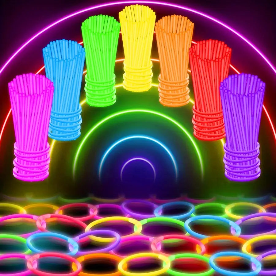 Bastones luminosos de neón a granel, collares y pulseras para fiestas en colores neón tipo arcoíris vibrantes, agrupados y dispuestos contra un fondo con un arco luminoso.