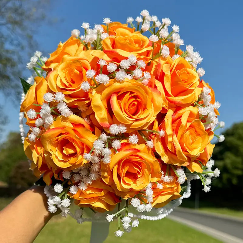 A vibrant bouquet of artificial orange roses accented with delicate white baby’s breath in a white silk rose wedding bouquet with lace and pearls.