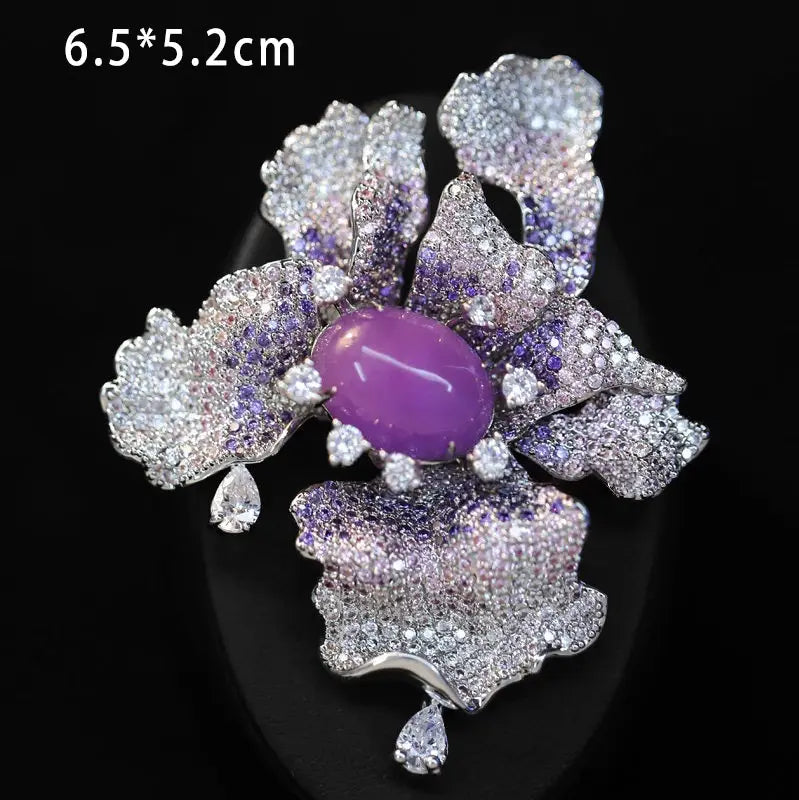 Broche de mariposa de zirconio púrpura brillante con un motivo central de piedra amatista ovalada, rodeada de pétalos intrincados con acabado en tono de plata, engastados con gemas claras y violetas, y realzada con cristales colgantes con forma de lágrima.