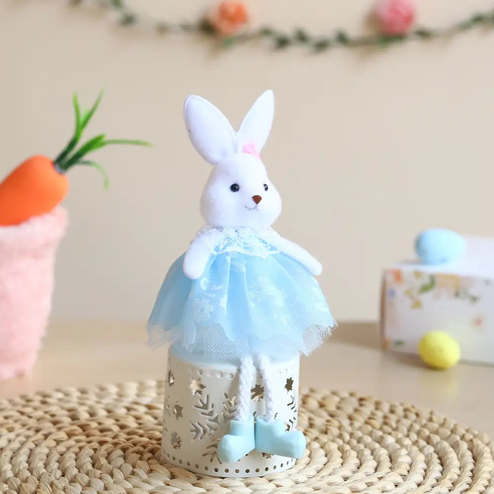Eine weiße Plüschhasen-Figur, gekleidet in einen hellblauen Tüll-Tutu und passende Stiefel, sitzt auf einer dekorativen zylindrischen Laterne aus dem Oster-Feen- und Osterhasen-Anhängeset.