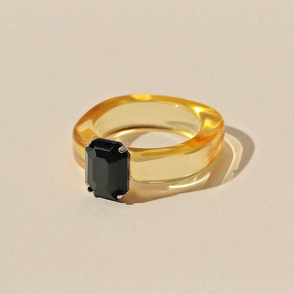 A colorful resin crystal geometric ring for women featuring a sleek translucent amber band with a bold black emerald-cut stone set in silver prongs.