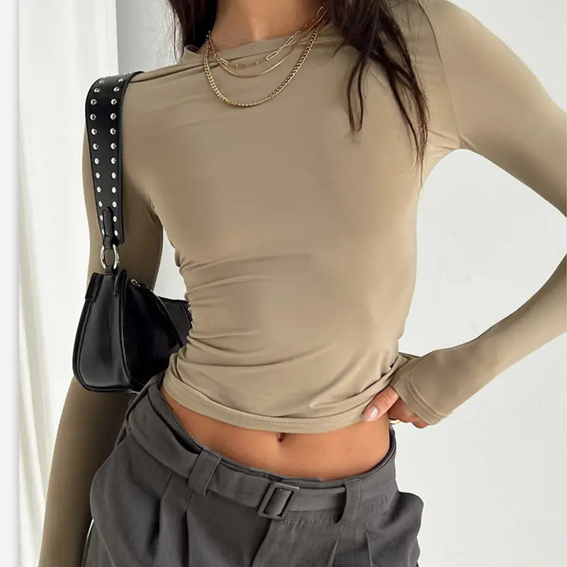 Blusa corta ajustada tipo slim fit beige para mujer, con mangas largas fruncidas, confeccionada con material semitransparente, silueta entallada y dobladillo fruncido.