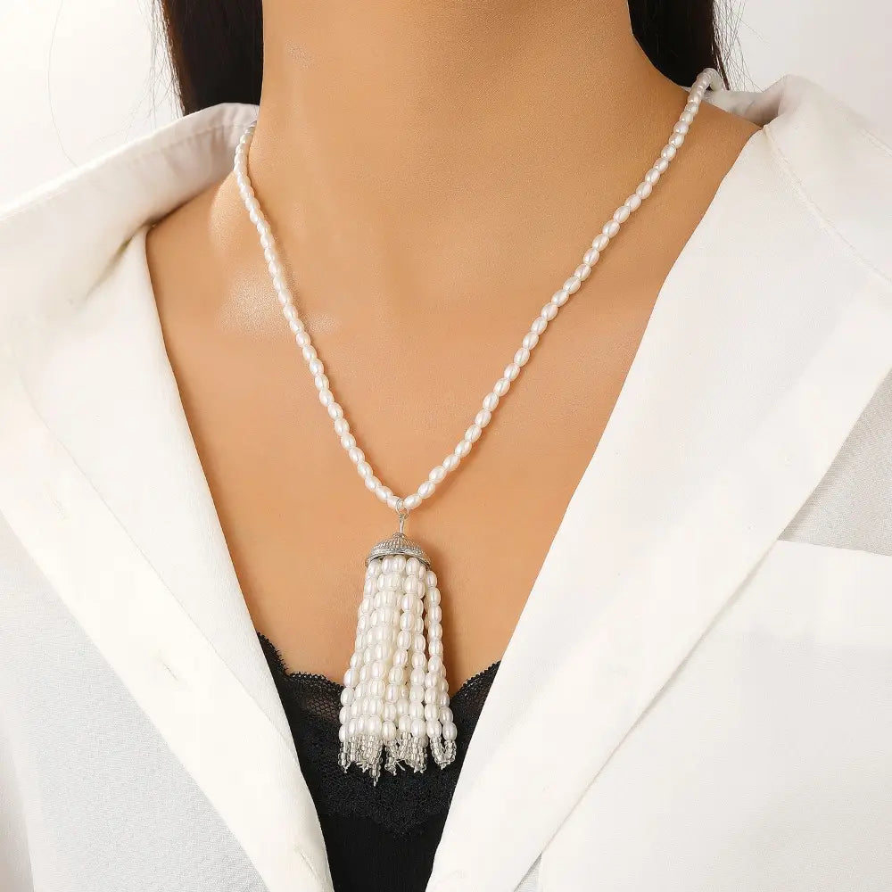 Collier-ras-de-cou élégant en perles blanches avec pendentif à pompon, composé d’une chaînette délicate et d’une fermeture argentée brillante, conçu comme une longue chaîne de pull-over.
