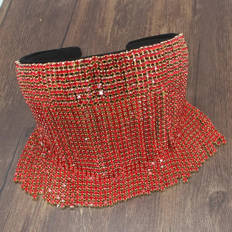 Ceinture corset éblouissante, rehaussée de cristaux rouges, avec intérieur en velours noir et accents en métal ton doré, présentée aux côtés d’un serre-tête en perles et strass pour mariée élégant.