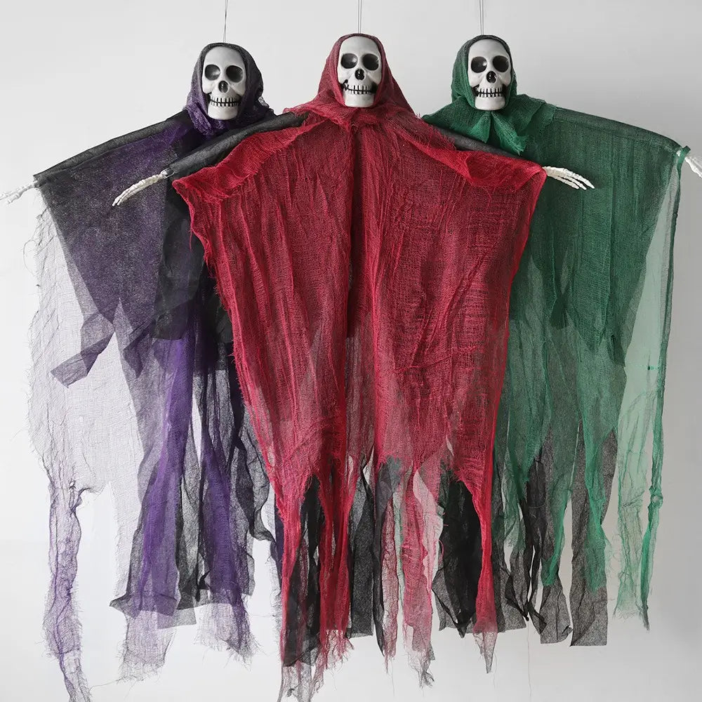 Trois décorations d’Halloween de fantôme squelettique suspendu, des squelettes pendants, drapés dans des manteaux en tissu déchiré violet, rouge et vert, avec des visages et des bras squelettiques blancs.
