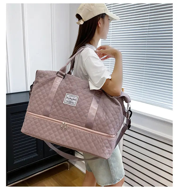 Bolsa de viaje tipo duffel acolchada grande color rosa suave con correa para el hombro a juego y una etiqueta rectangular en el frente, diseñada como tote weekender.