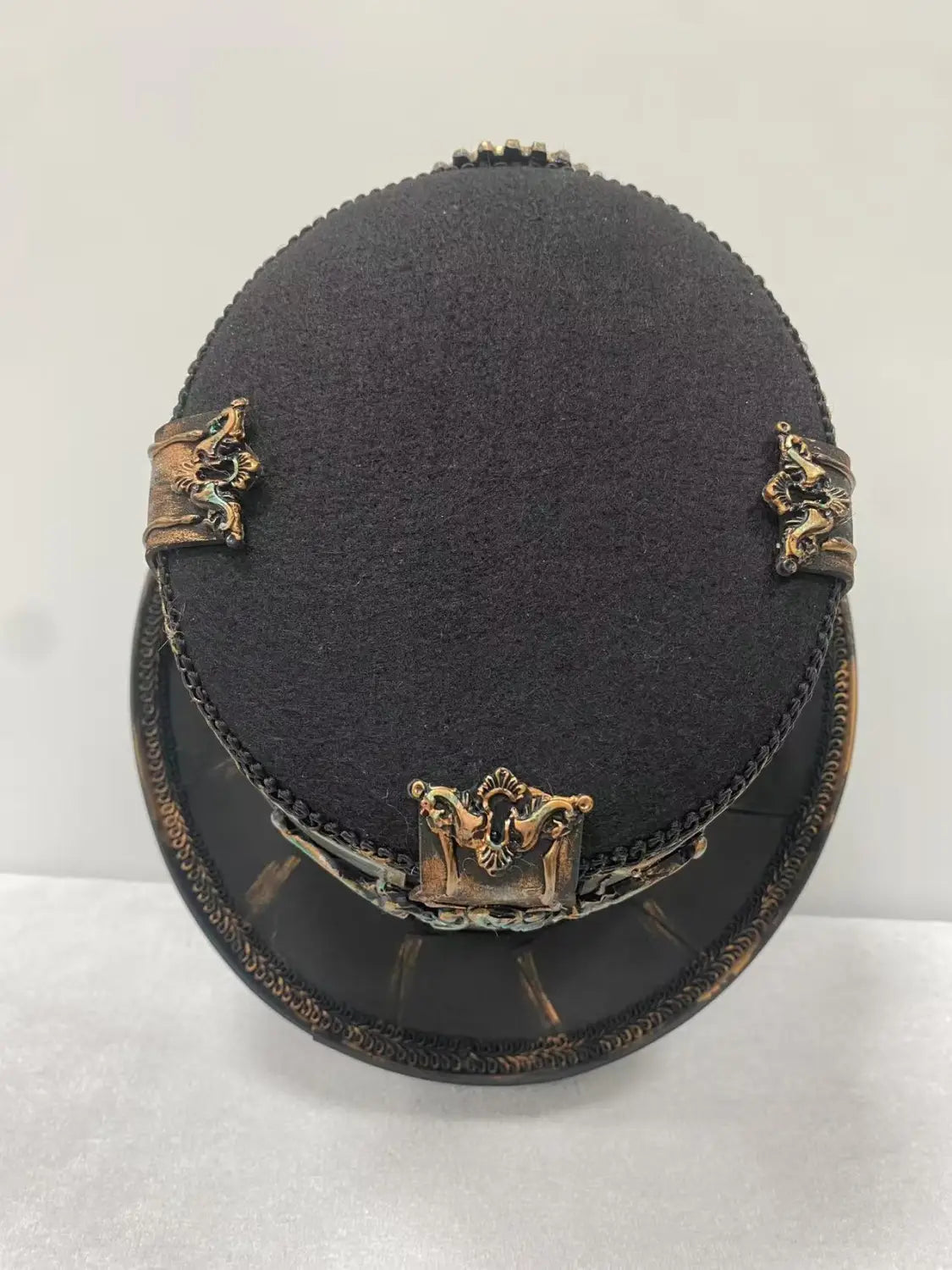 Steampunk top hat in black felt featuring ornate gold-toned metal embellishments and a decorative clasp suitable for costume or fashion use.