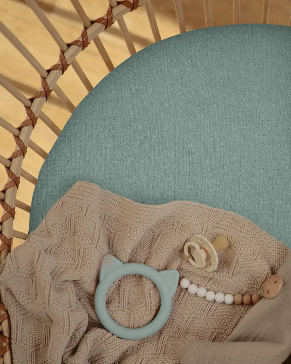 ein hellblauer Silikon-Beißring in Katzenform, ausgestellt, mit einem Babybettlaken-Set aus Baumwollmuslin, das für den Komfort und die Sicherheit von Säuglingen entwickelt wurde.