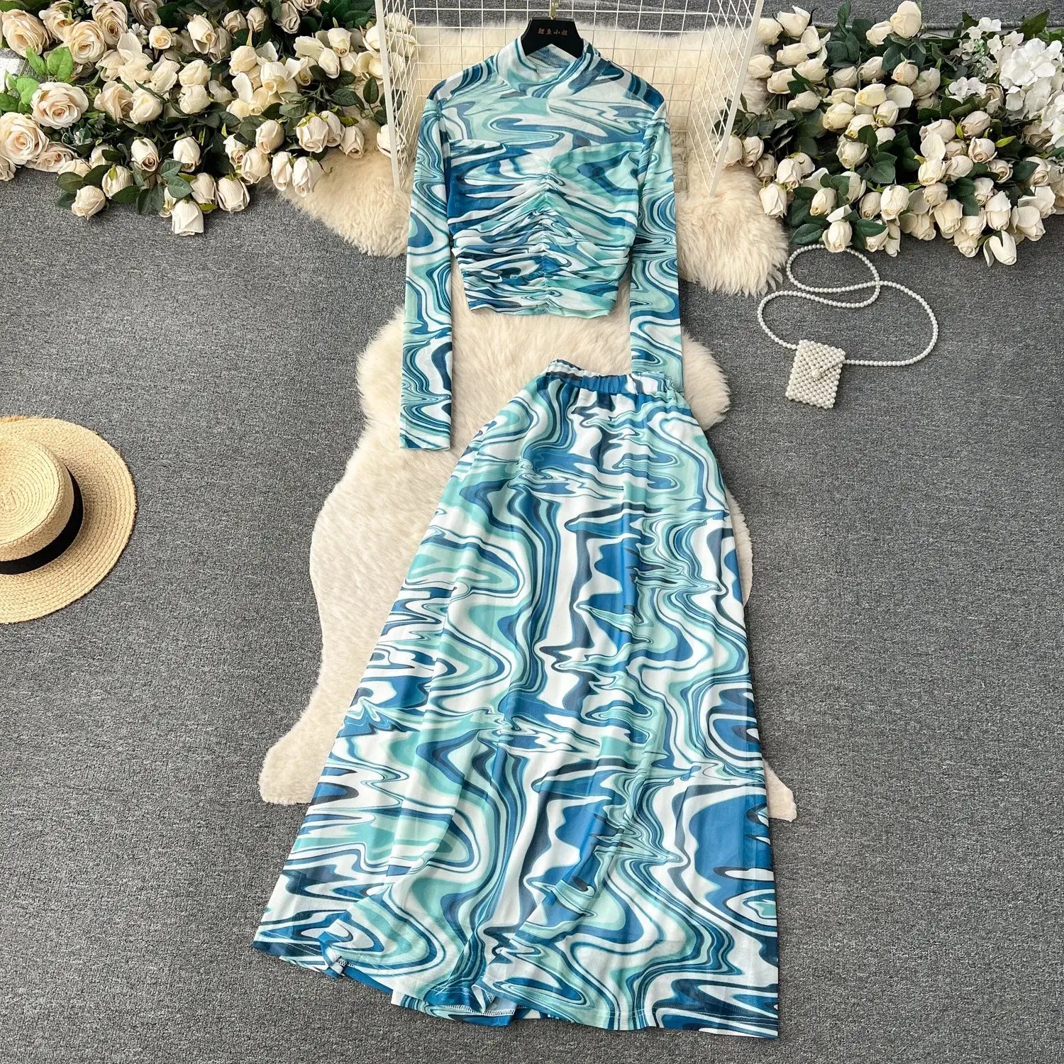 a two-piece mesh skirt set with a high-neck long-sleeved top and matching maxi skirt featuring a marble print in shades of blue teal and white with an elastic closure type