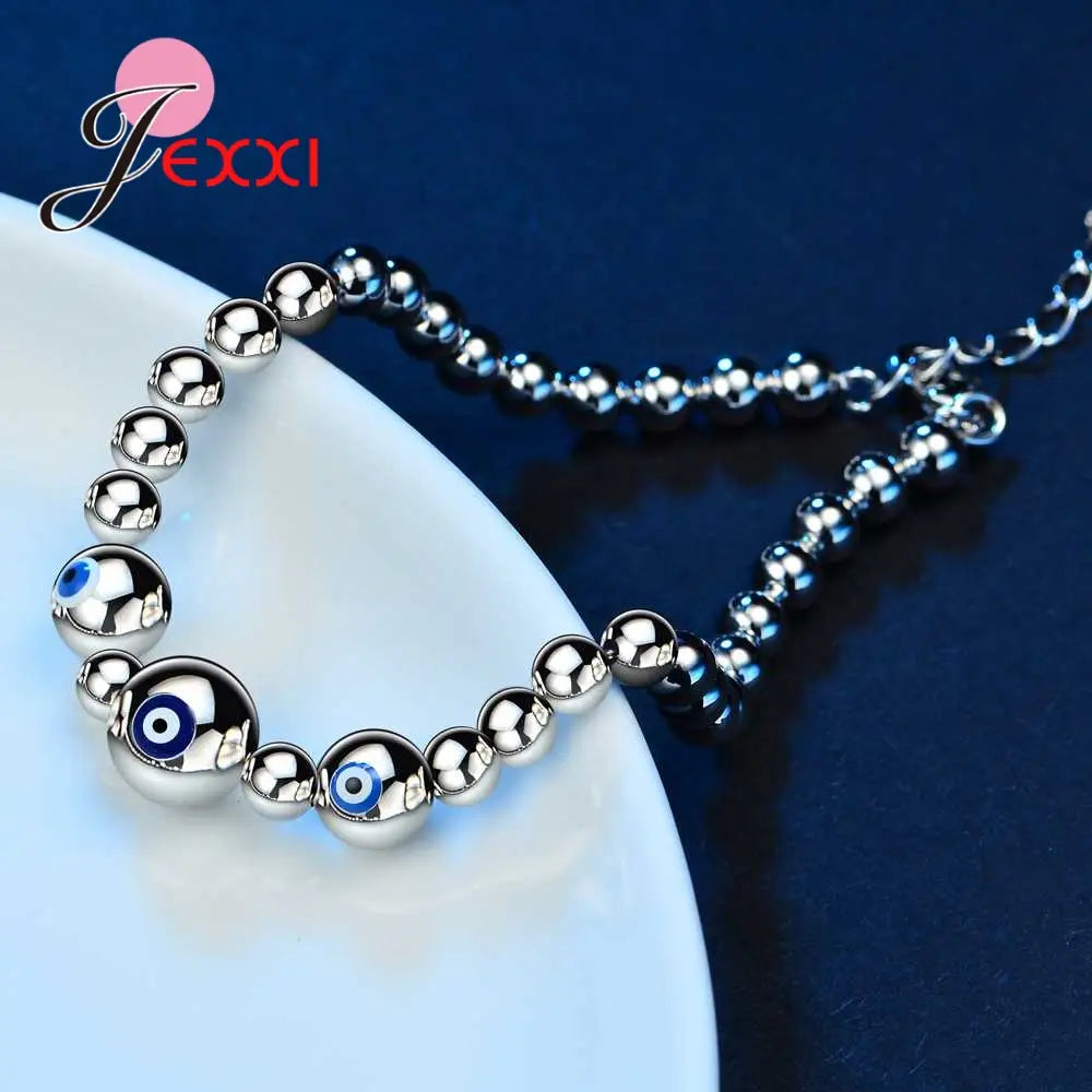 Sterling silver evil eye charm bracelet for women featuring a silver beaded anklet with polished spherical beads and three prominent blue evil eye charms.