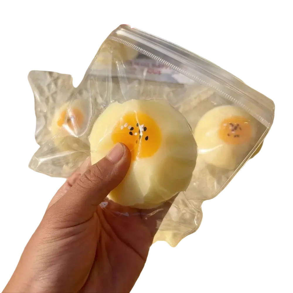 Soft pale yellow silicone egg yolk pastry squishy with bright orange yolk and black sesame seed details front view