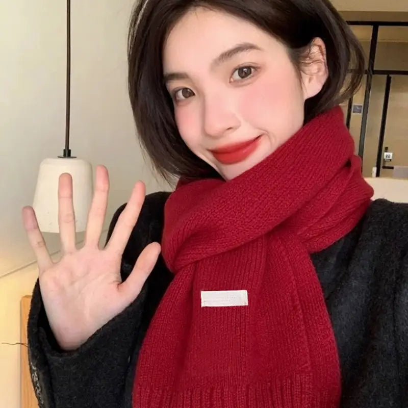 Una bufanda de invierno tejida en rojo, vibrante, para hombres y mujeres, con una sutil textura acanalada y una pequeña etiqueta rectangular blanca en la parte frontal.