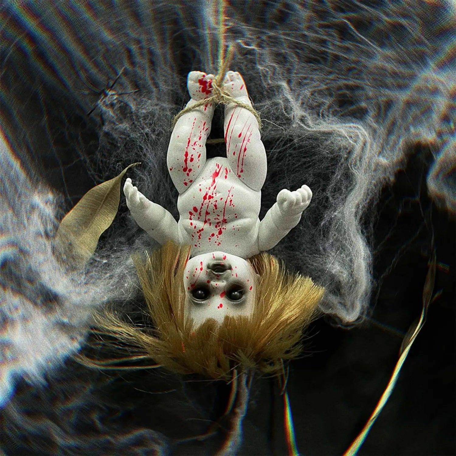A white porcelain halloween hanging ghost doll with blonde hair and red splatter details suspended by twine as a spooky prop.