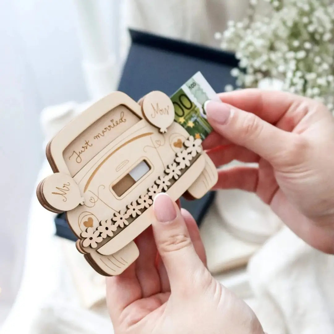 Eine hellfarbige Holzgeldbörse in Form eines Autos mit eingraviertem „Mr“ und „Mrs“ an den Seiten, dekorativen floralen Aussparungen und einem Währungsschlitz, entworfen als Geschenkbox aus Holz in Form eines Hochzeitswagens zum Aufbewahren von Geld.