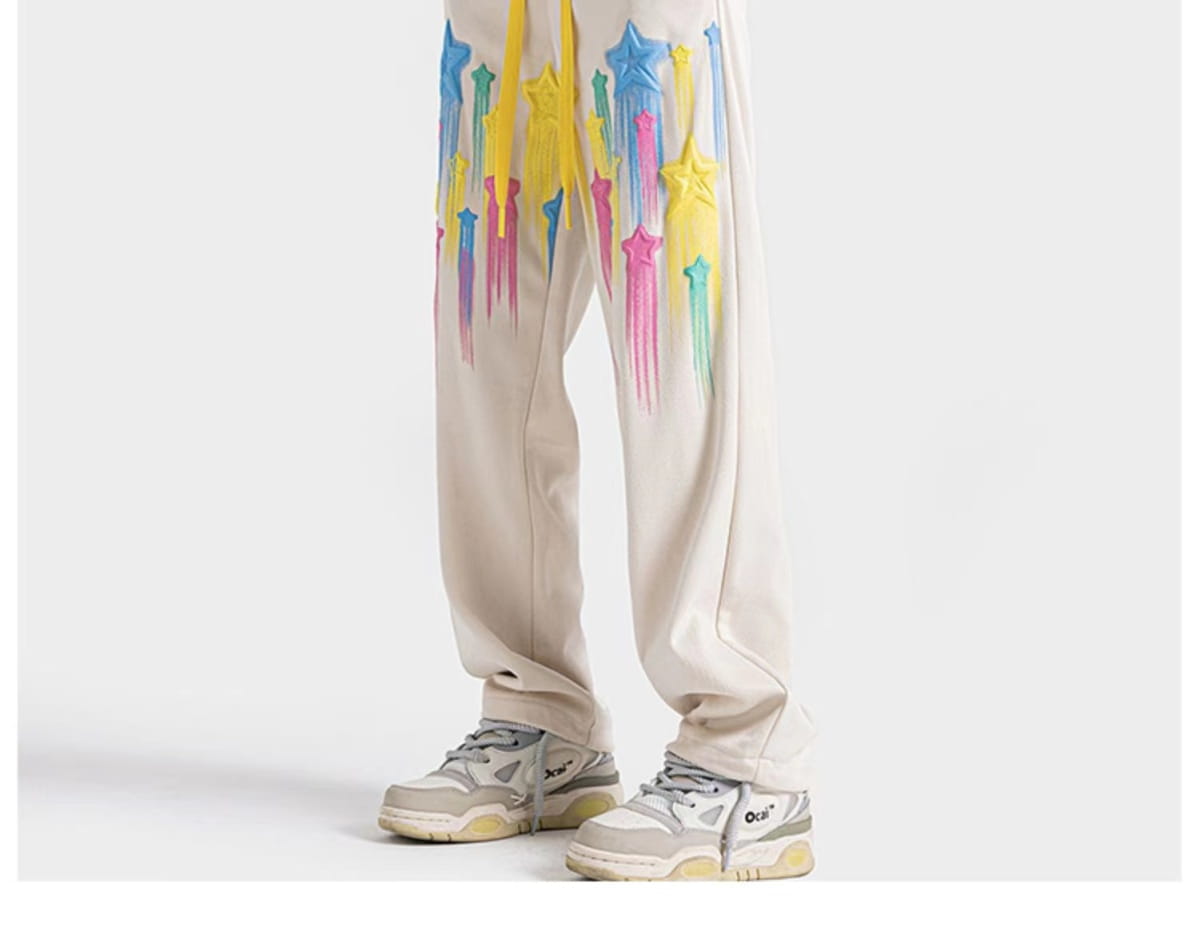 Beige sweatpants featuring vibrant dripping star graphics in blue yellow pink and green designed for men.
